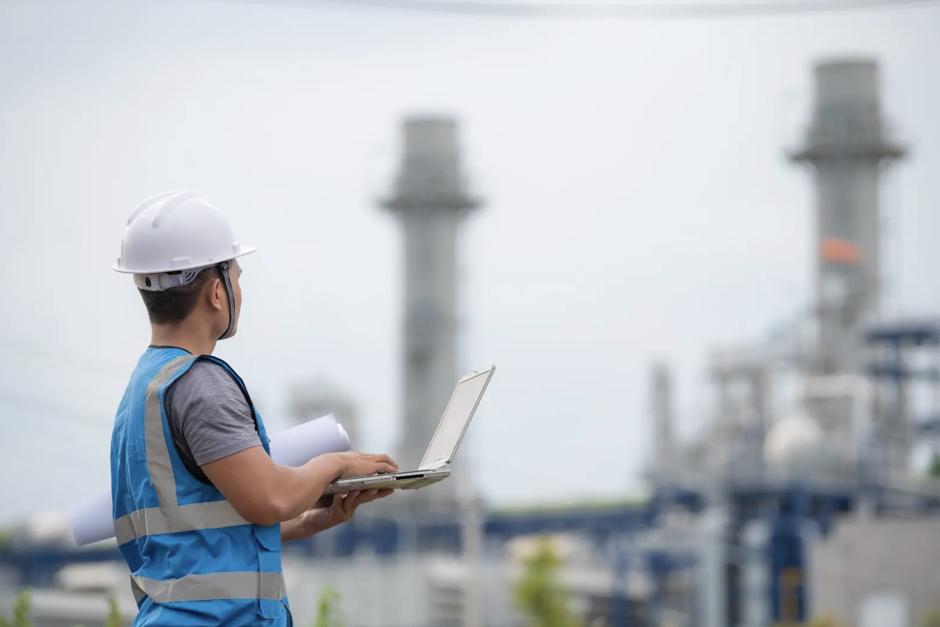 Construction worker in safety gear holding laptop at construction site.