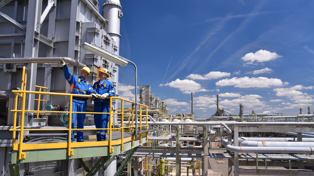 Two construction workers at a refinery discussing a project.